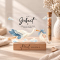 Geldgeschenk zur Geburt als Acryl-Aufsteller im Storchen-Design: Storch mit Baby im Tuch, Röhrchen mit Geldschein