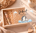 Geldgeschenk zur Geburt in Holzkiste im Pinguin-Design, Deckel halb offen, Reagenzglas mit Geldschein in Holzwolle