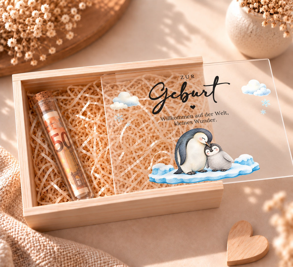 Geldgeschenk zur Geburt in Holzkiste im Pinguin-Design, Deckel halb offen, Reagenzglas mit Geldschein in Holzwolle