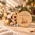 Offene Keksdose aus Glas mit Weihnachtsplätzchen, daneben lehnt der bedruckte Bambusdeckel „Ein Glas voll Weihnachtsglück“ mit Wichtel