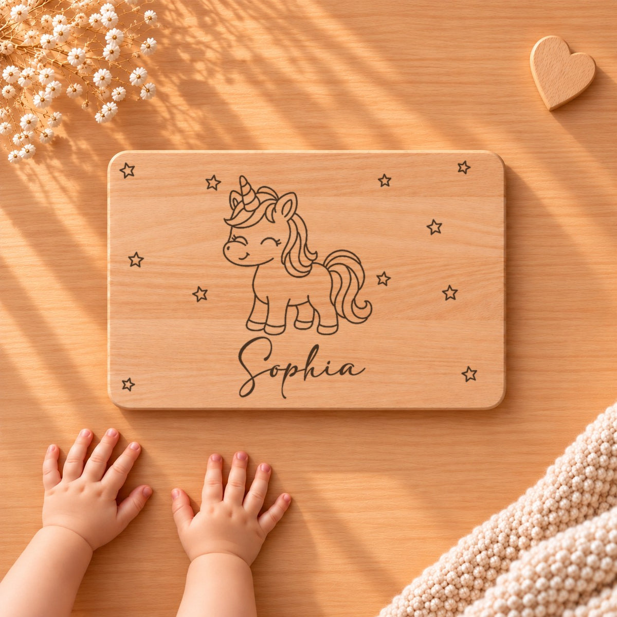 Personalisiertes Frühstücksbrettchen aus Buche mit einem Einhorn, Sternen und Namen Sophia, daneben Babyhände
