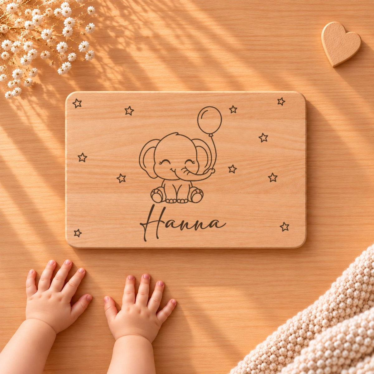 Personalisiertes Frühstücksbrettchen aus Buche mit einem Elefanten mit Luftballon, Sternen und Namen Hanna, daneben Babyhände