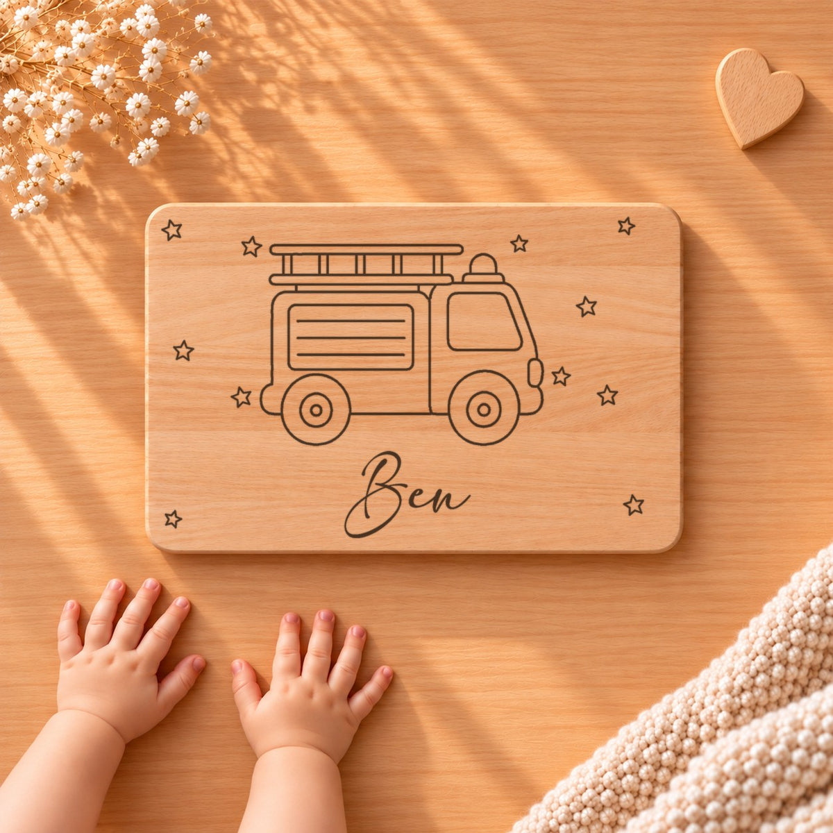 Personalisiertes Frühstücksbrettchen aus Buche mit einem Feuerwehrauto, Sternen und Namen Ben, daneben Babyhände
