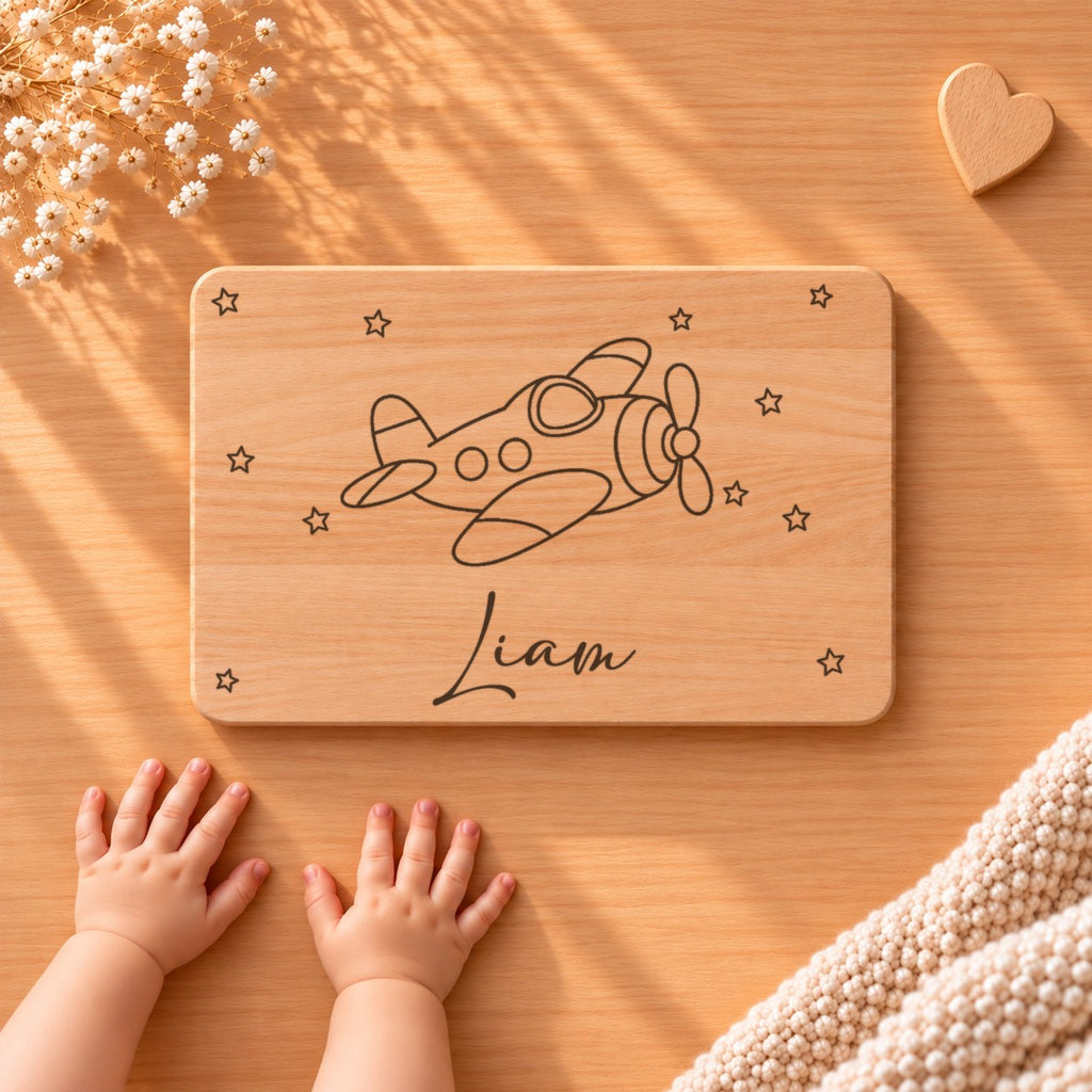 Personalisiertes Frühstücksbrettchen aus Buche mit einem Flugzeug, Sternen und Namen Liam, daneben Babyhände