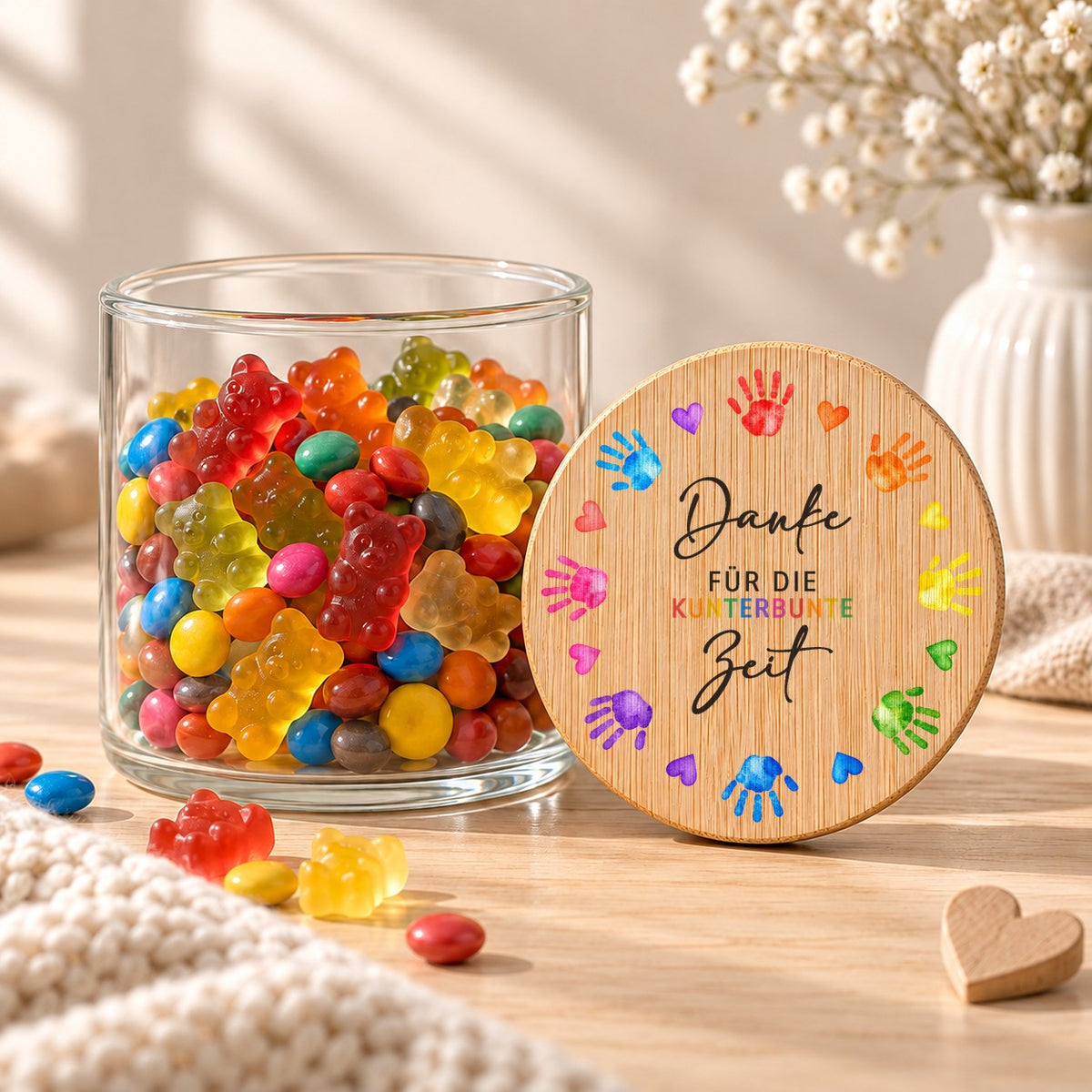Offenes Vorratsglas mit Gummibärchen, daneben lehnt der Deckel „Danke für die kunterbunte Zeit“, Design Kinderhände