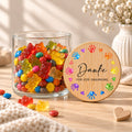 Offenes Vorratsglas mit Gummibärchen, daneben lehnt der Deckel „Danke für jede Umarmung“