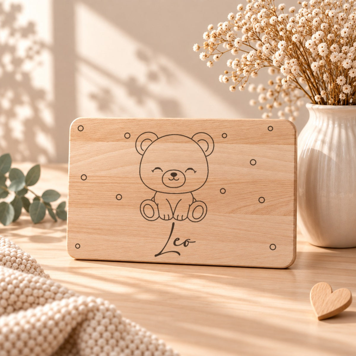 Personalisiertes Frühstücksbrettchen aus Holz mit graviertem Bären, Namen und kleinen Kreisen, aufgestellt neben Schleierkraut