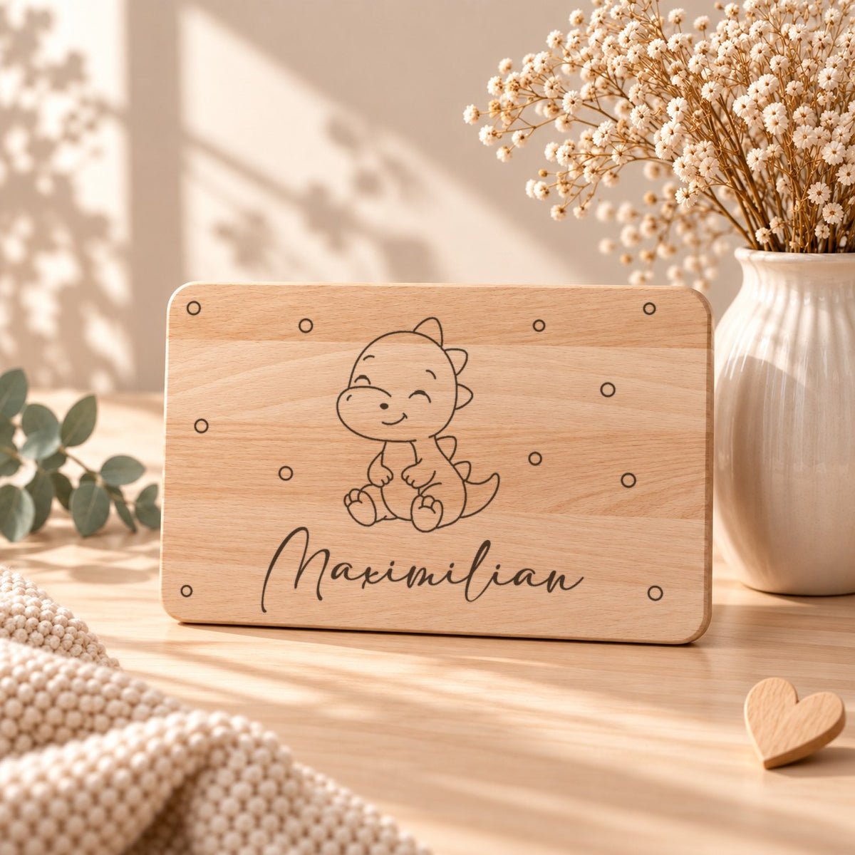 Personalisiertes Frühstücksbrettchen aus Holz mit graviertem Dino, Namen und kleinen Kreisen, aufgestellt neben Schleierkraut