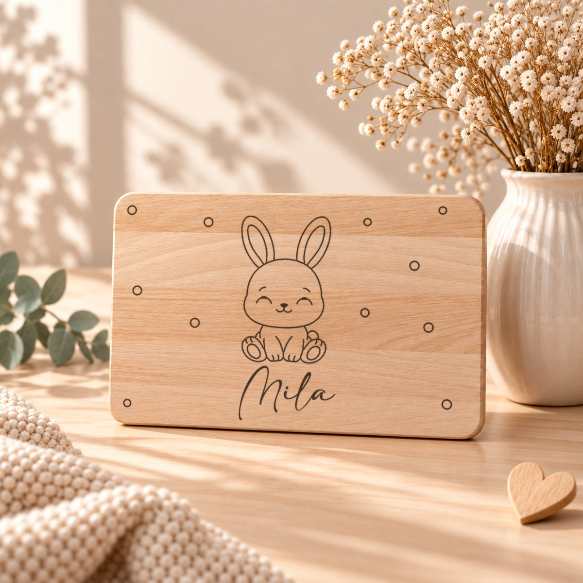 Personalisiertes Frühstücksbrettchen aus Holz mit graviertem Hasen, Namen und kleinen Kreisen, aufgestellt neben Schleierkraut