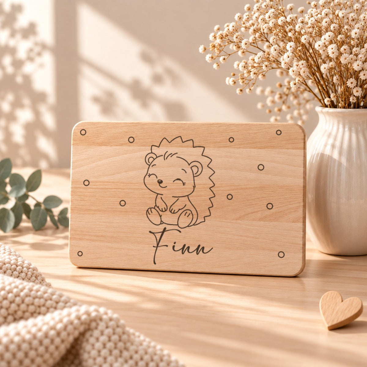Personalisiertes Frühstücksbrettchen aus Holz mit graviertem Igel, Namen und kleinen Kreisen, aufgestellt neben Schleierkraut