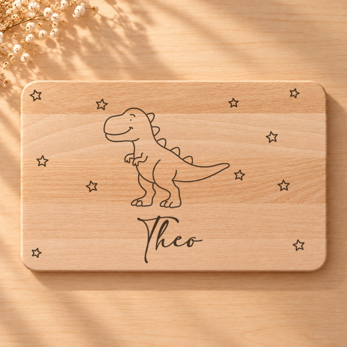 Nahaufnahme der Lasergravur: T-Rex und der Name Theo in Schreibschrift auf hellem Holz