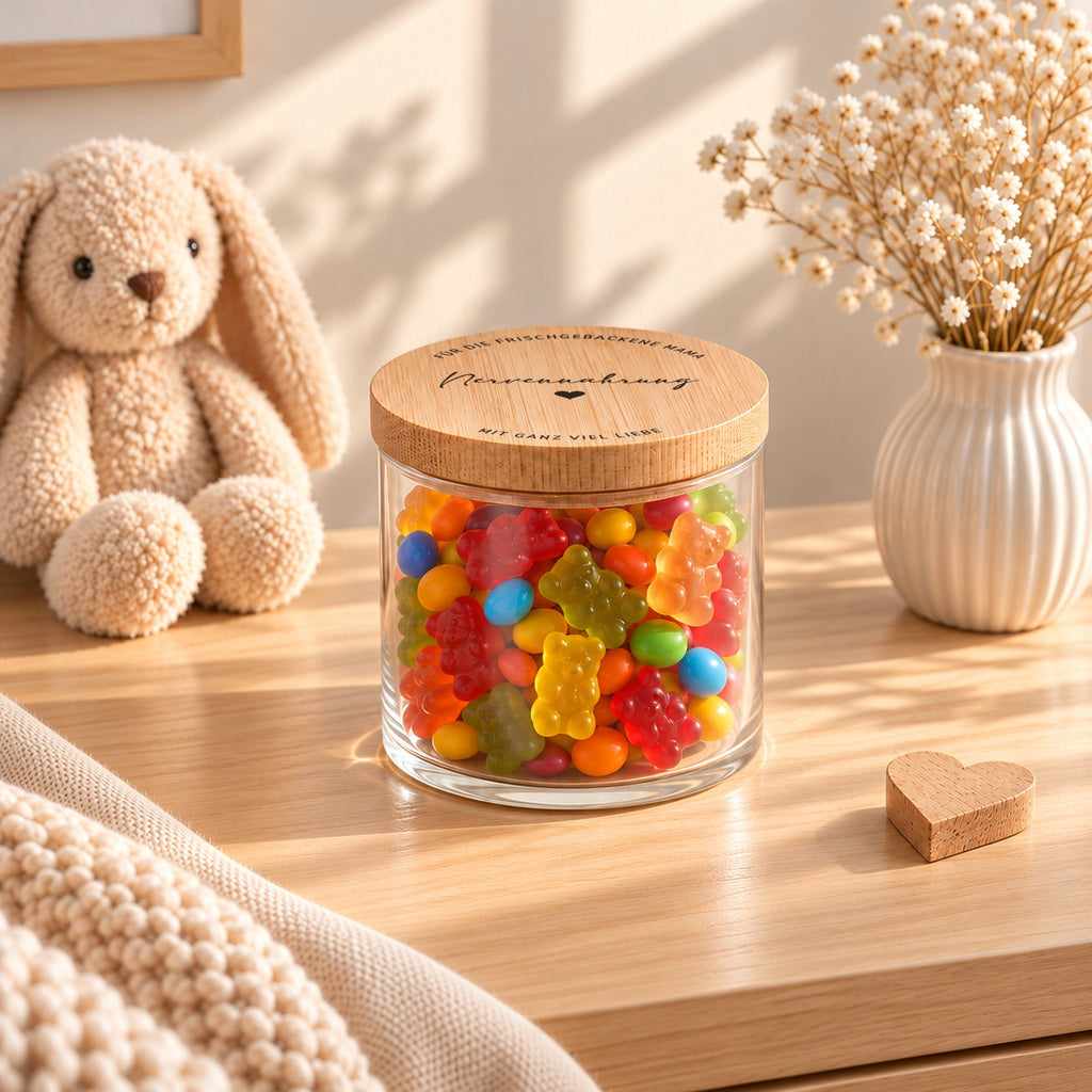 Vorratsglas mit Spruch-Deckel „Nervennahrung – für die frischgebackene Mama – mit ganz viel Liebe“ auf einem hellen Sideboard neben Kuschelhase und Trockenblumen