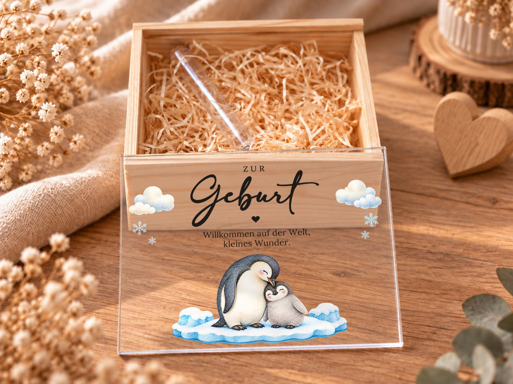 Geöffnete Holzkiste mit Holzwolle und Reagenzglas, Deckel im Pinguin-Design davor