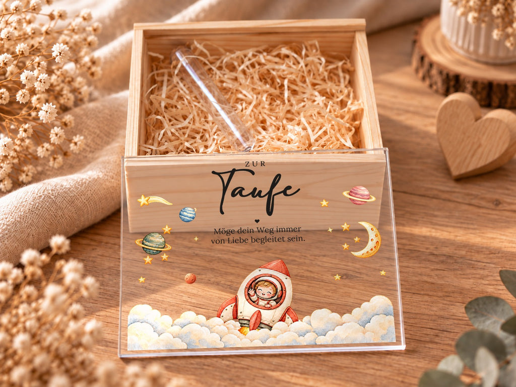 Offene Taufkiste mit Holzwolle und Reagenzglas, Acryldeckel mit Rakete davor