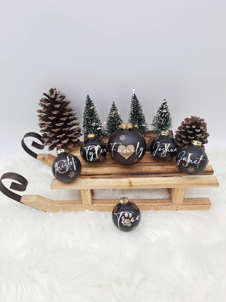 Personalisierte dunkle Weihnachtskugeln mit Familiennamen und Schneeflocken auf einem Holzschlitten