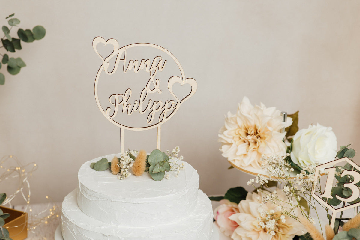 Runder personalisierter Caketopper zur Hochzeit neben Blumen und Tischnummer